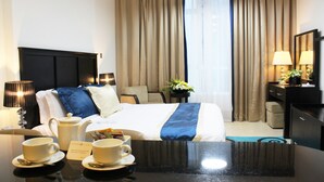 Une chambre d’hôtel comprenant un lit, une table de chevet, des lampes, un bureau avec une chaise et une fenêtre avec des rideaux.