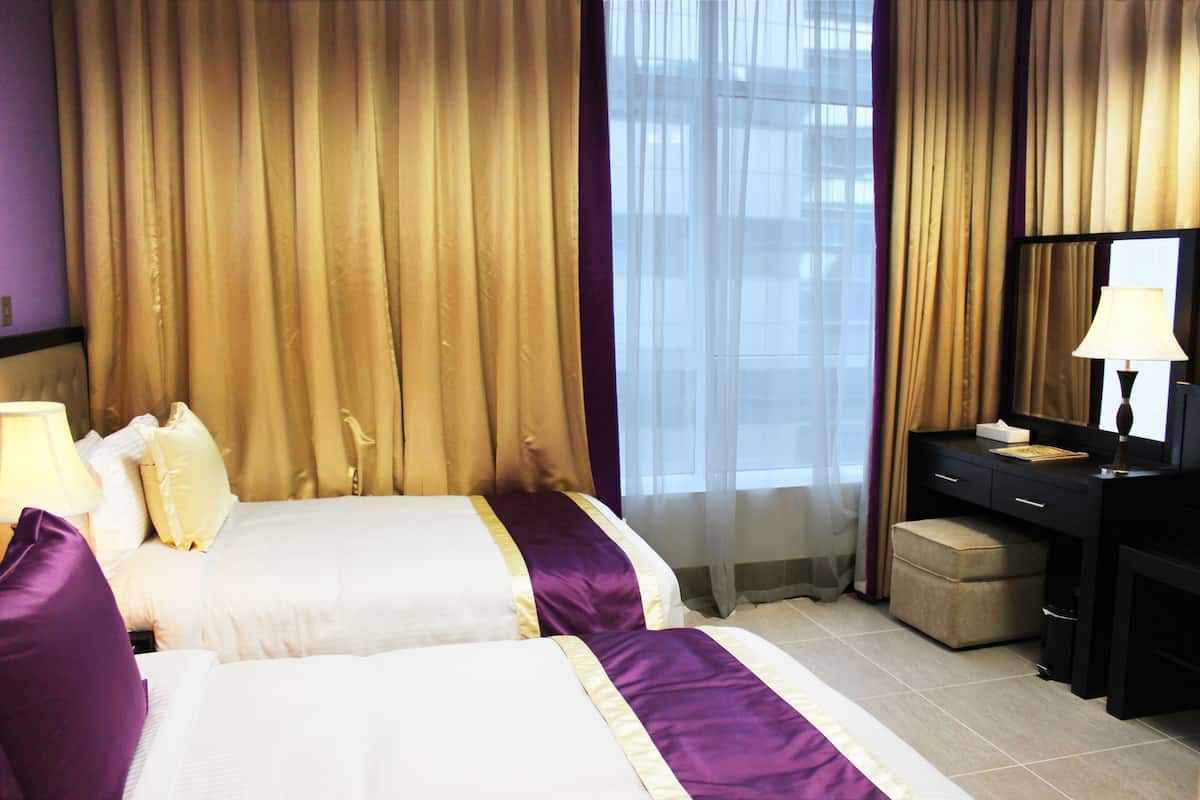 Une chambre d’hôtel avec deux lits, un bureau, une chaise et une fenêtre avec des rideaux.