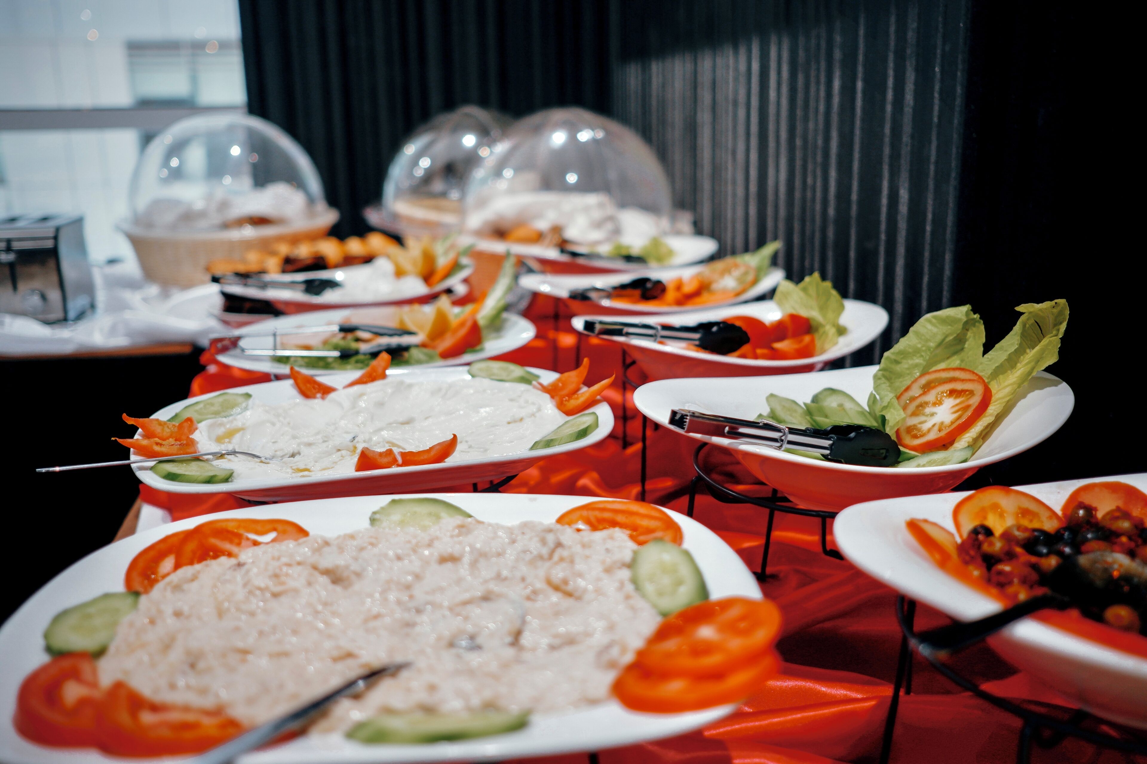 Una mesa de buffet con diversos platos, como arroz, ensaladas y verduras, cubierta con un mantel rojo.