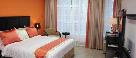 A hotel room with a bed, a desk, a chair, a TV, and a window with curtains.