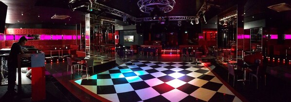 Zona de bar con suelo a cuadros, asientos rojos y cabina para DJ.