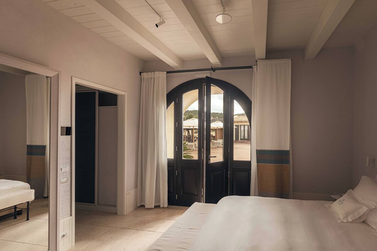 A hotel room with a bed, a desk, and a view of the outdoor area through a glass door.