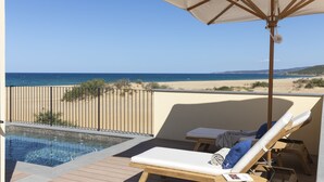 Un balcón con piscina, sillones de descanso y vista a la playa y al océano.