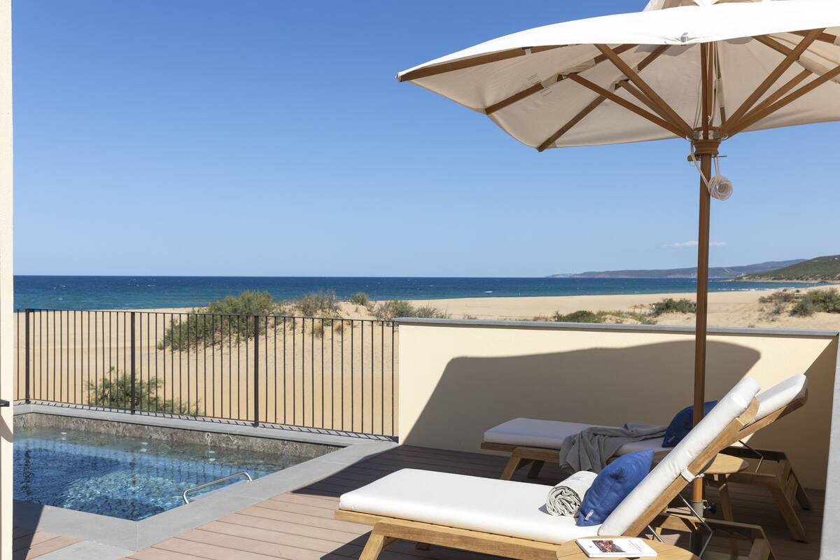 A balcony with a pool, lounge chairs, and a view of the beach and ocean.