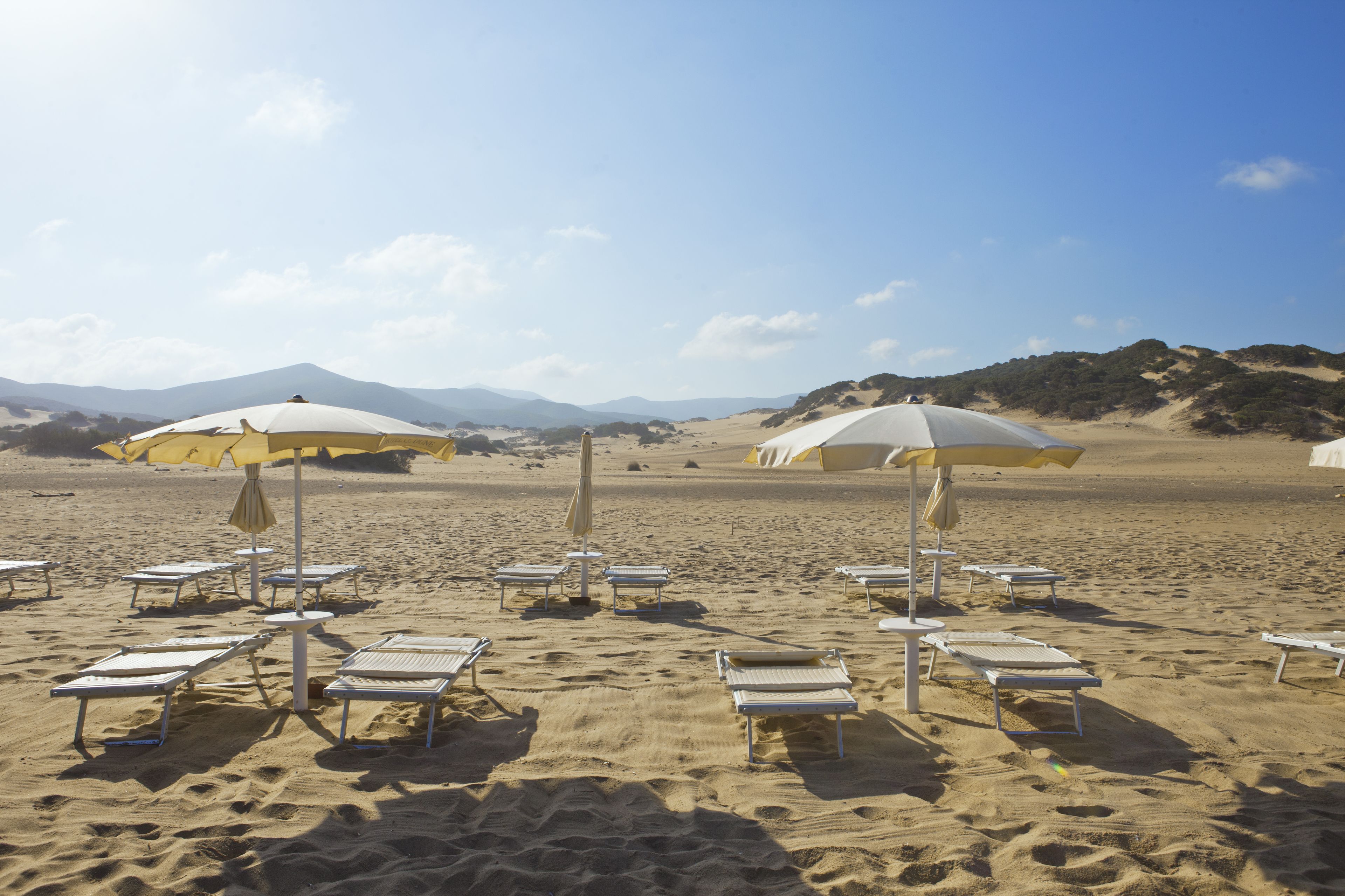A beach with white lounge chairs and umbrellas, a clear sky, and distant mountains.