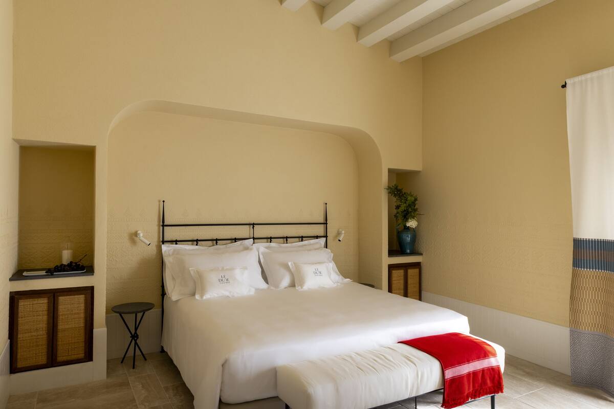 A bedroom with a bed, a small bedside table, a nightstand, and a window with curtains.