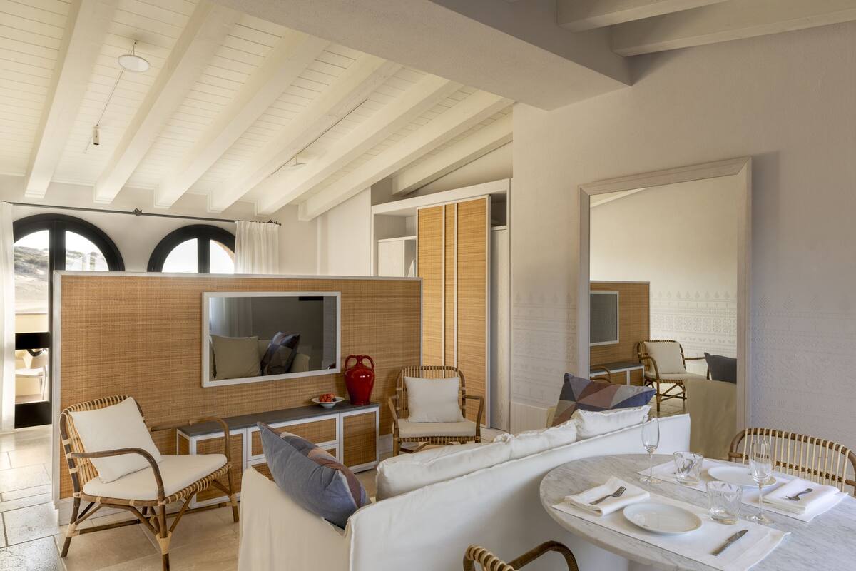 A spacious living area with a high ceiling, a large TV, wicker furniture, and a dining table set for four.