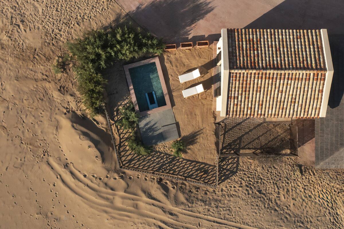 An aerial view of a desert resort with a swimming pool, lounge chairs, and a shaded area.
