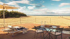 Un área de descanso en la playa con piscina, sillas de descanso y una mesa con bebidas.
