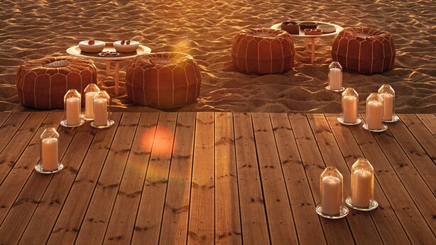Terraza de madera con cojines redondos y candelabros, dispuesta para disfrutar de la puesta de sol.