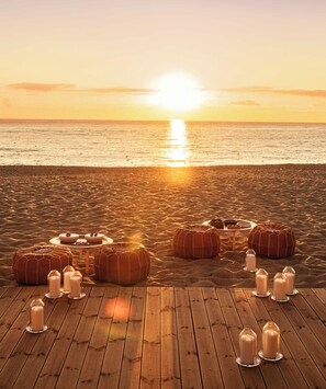 A wooden deck with round cushions and candle holders arranged for a sunset view. - Hotel Le Dune Piscinas (Arbus)