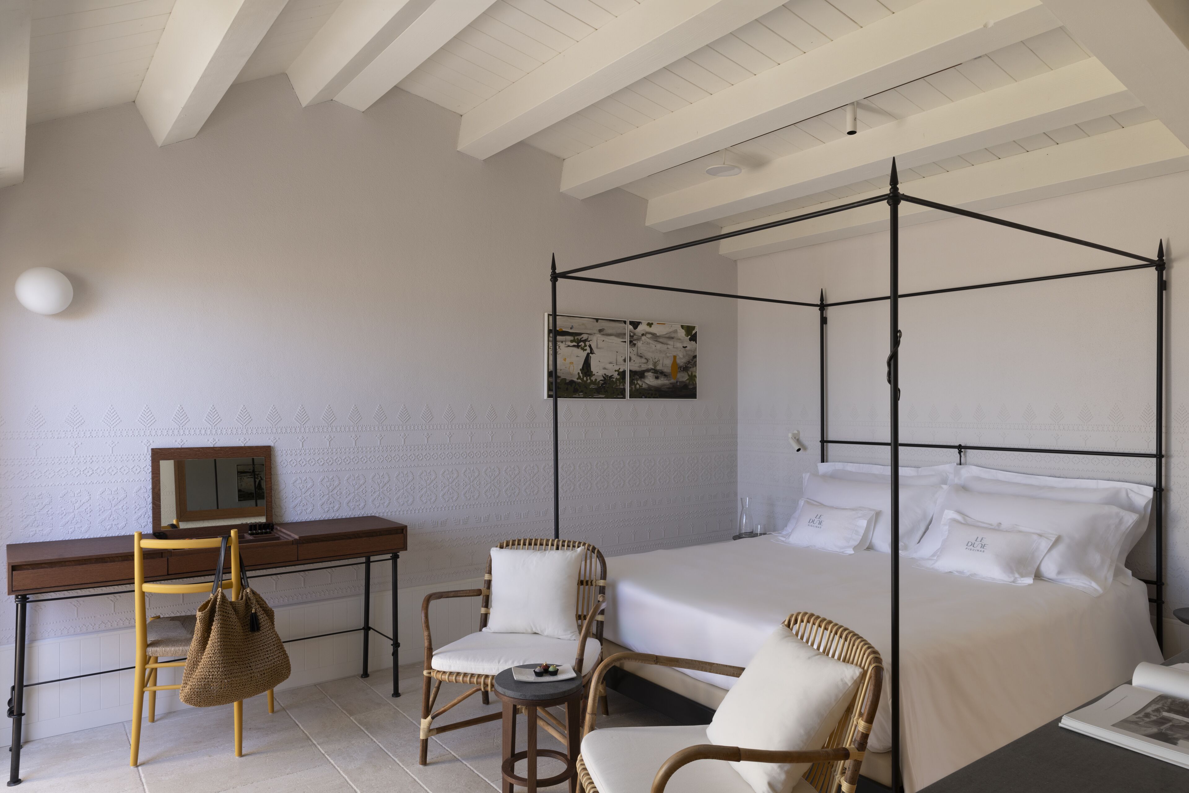 A bedroom with a four-poster bed, a desk with a chair, and two wicker chairs.