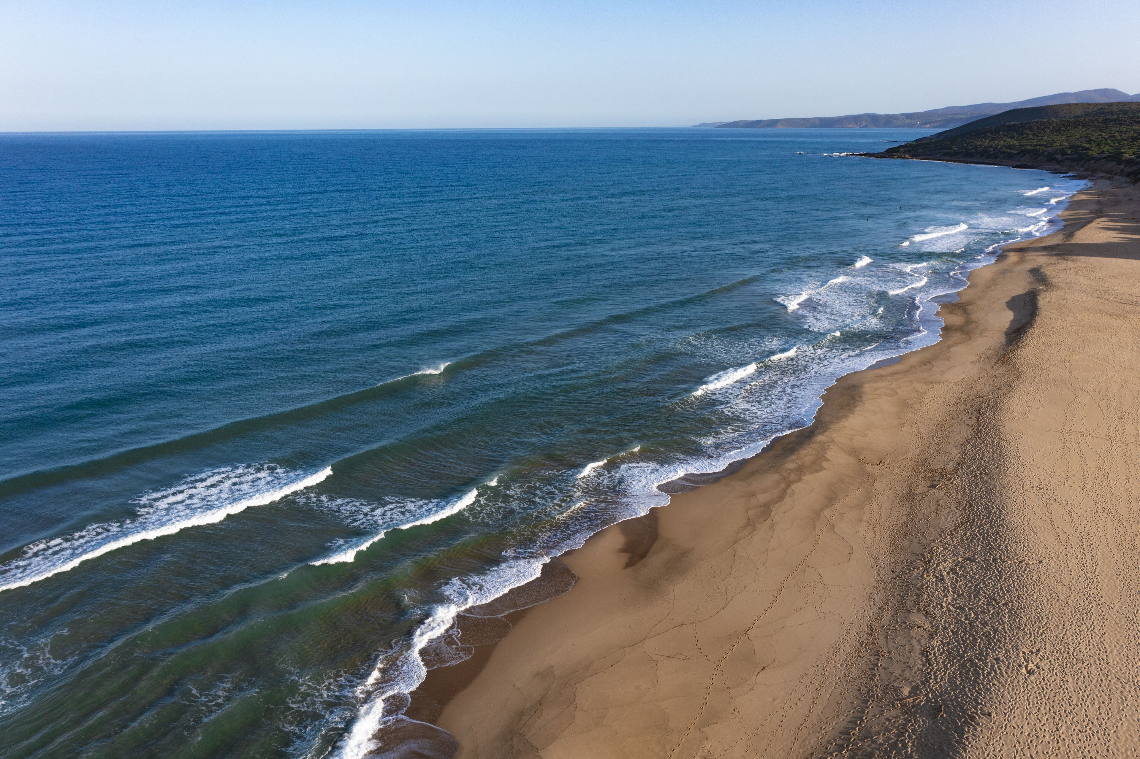 A beach with clear blue water and a sandy shore.