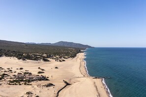 A coastal landscape with a sandy beach, a small building, and a mountain in the background. - Hotel Le Dune Piscinas (Arbus)