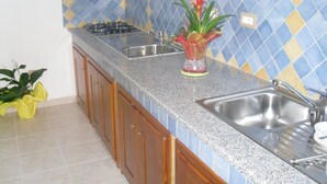 A kitchen with a granite countertop, stainless steel sink, and a backsplash with blue and yellow tiles. - Sa Marina (Siniscola)