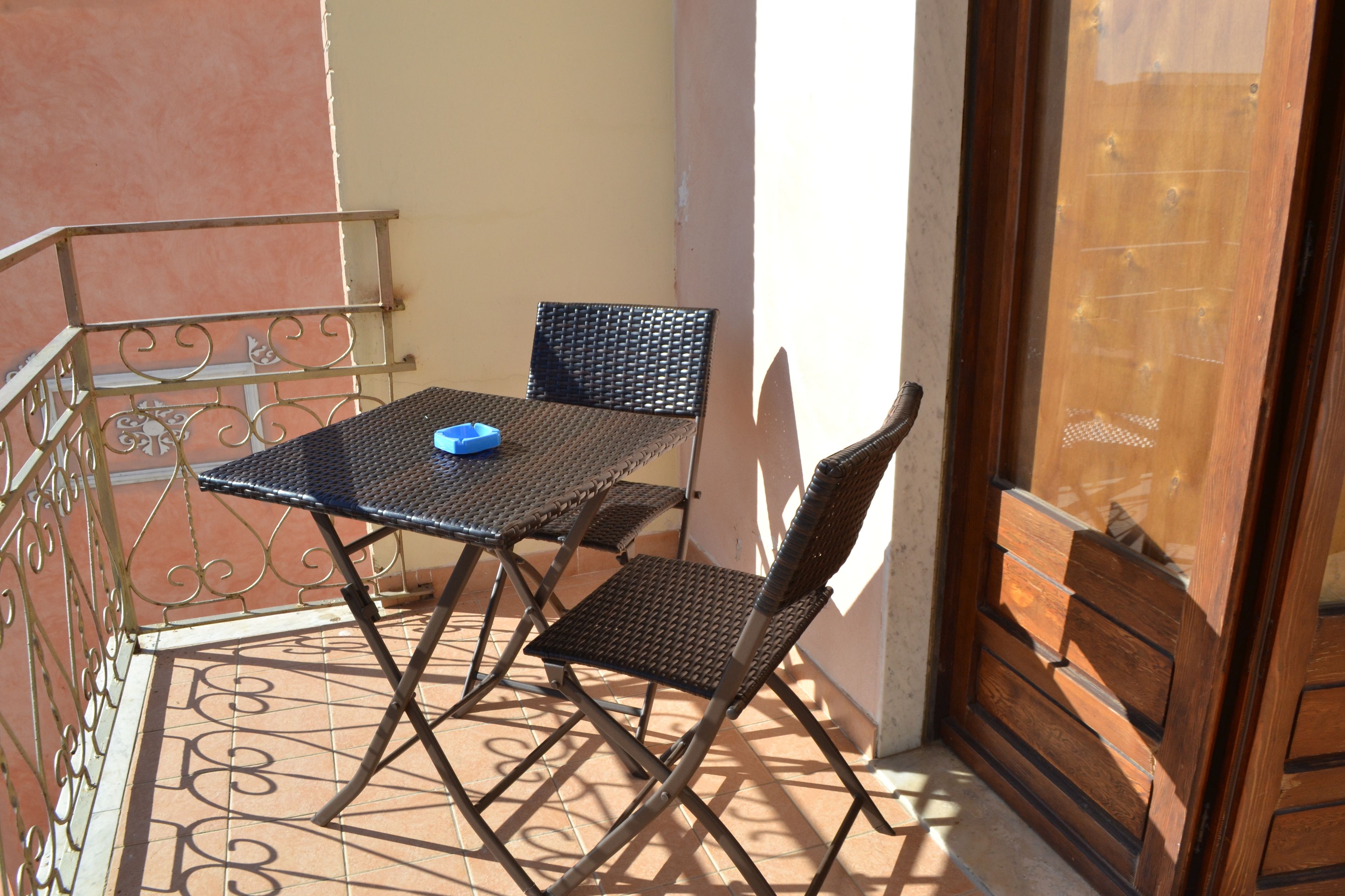 Ein kleiner Balkon mit Tisch und zwei Stühlen, einem Metallgeländer und einer Holztür.