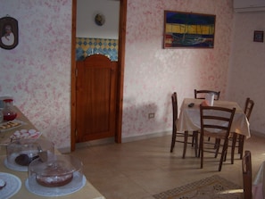 A dining area with a wooden door, a tiled backsplash, a painting on the wall, and a table set for four with chairs. - Sa Marina (Siniscola)
