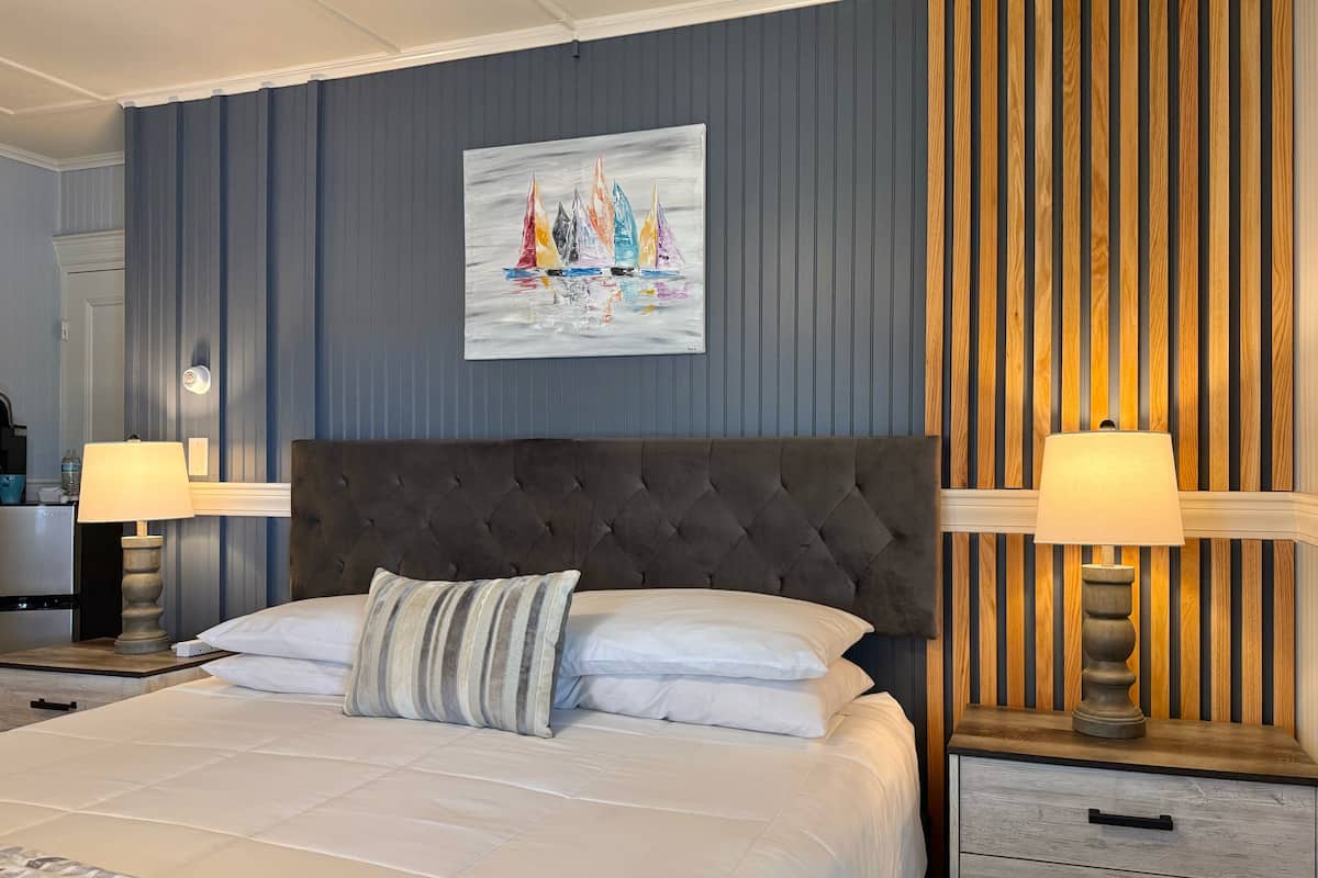 A bedroom with a large bed, two bedside tables with lamps, a wall-mounted painting, and a wooden panel wall.