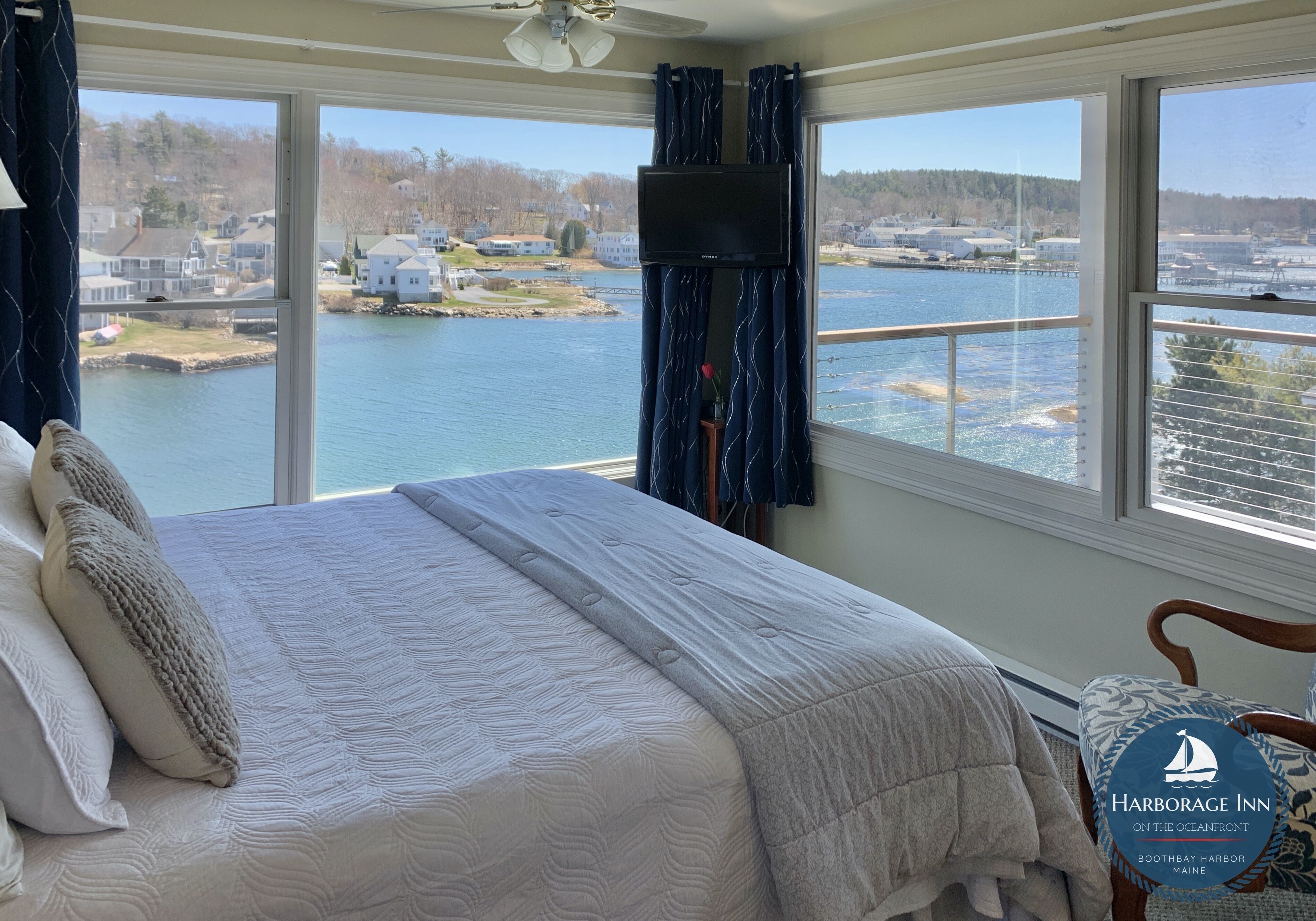 Une chambre avec un grand lit, un téléviseur fixé au mur et une vue sur un lac et des maisons.