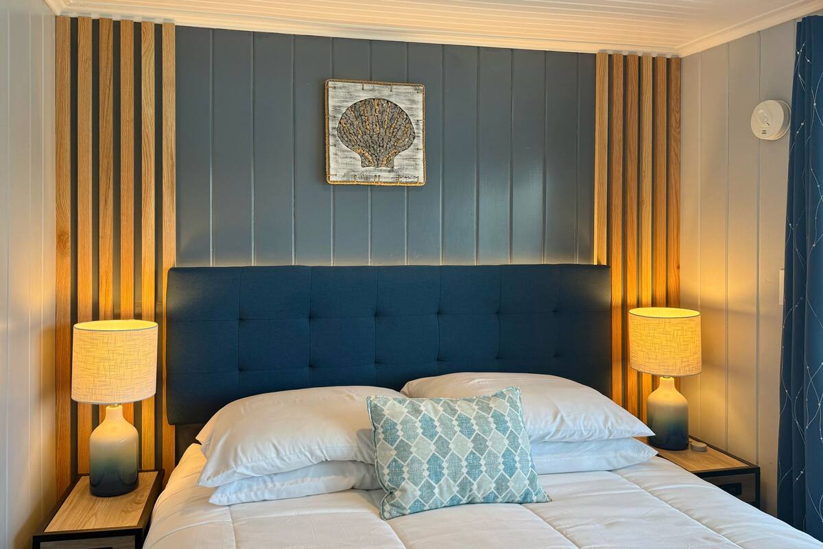 A neatly made bed with a blue headboard, two bedside lamps, and a decorative wall piece.