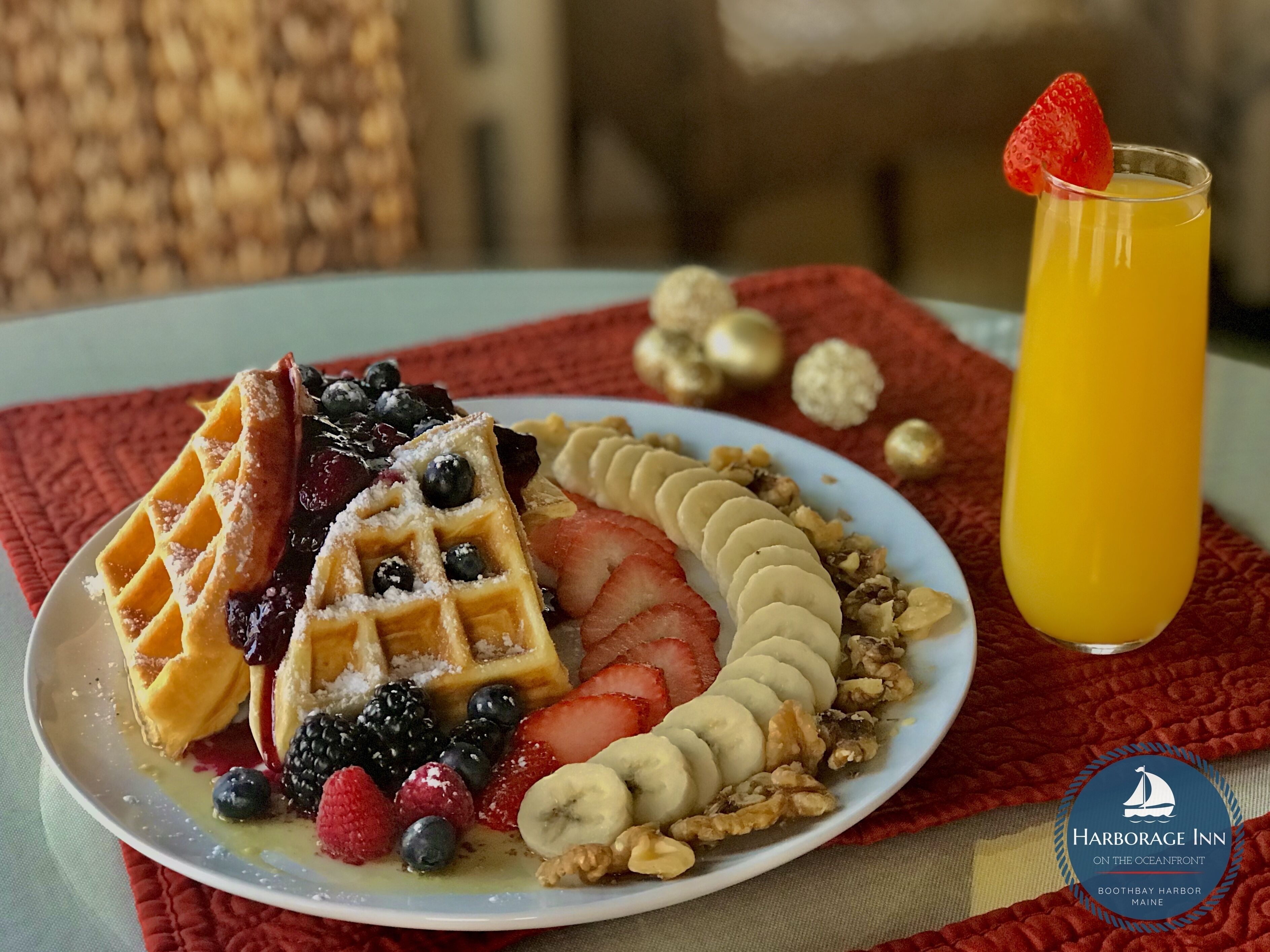 Prato de café da manhã com waffles, morangos, mirtilos, bananas e nozes, acompanhado de um copo de suco de laranja.