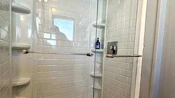 Un baño moderno con azulejos blancos tipo metro, cerramiento de ducha de vidrio y una botella de champú a la vista.