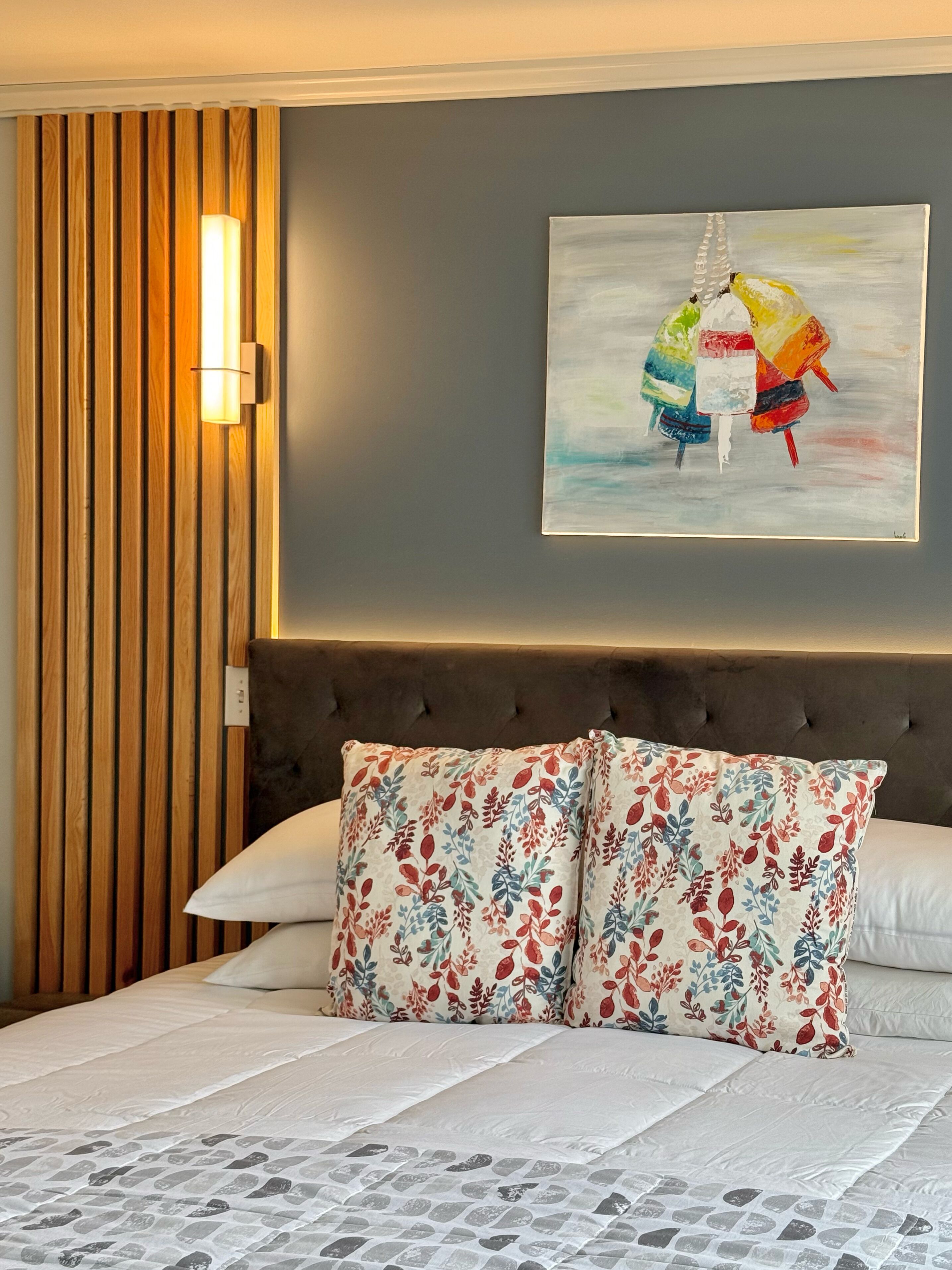 A bedroom with a bed, a wooden panel wall, a painting, and a light fixture.