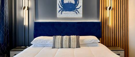 A modern hotel room with a large bed, a blue headboard, a wall-mounted artwork of a crab, and vertical wooden slats on one wall.