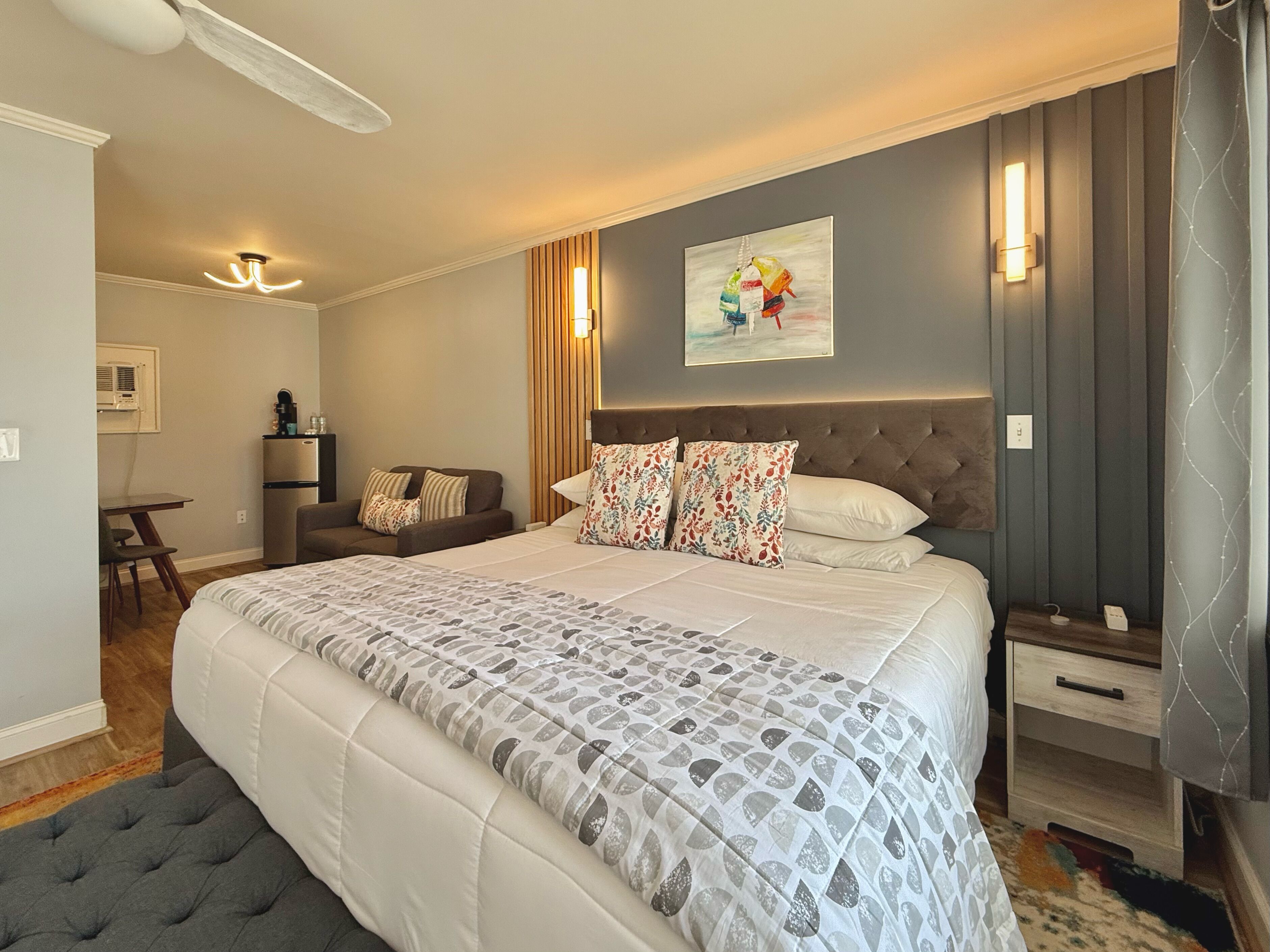 A modern hotel room with a large bed, a desk, a chair, and a small table.