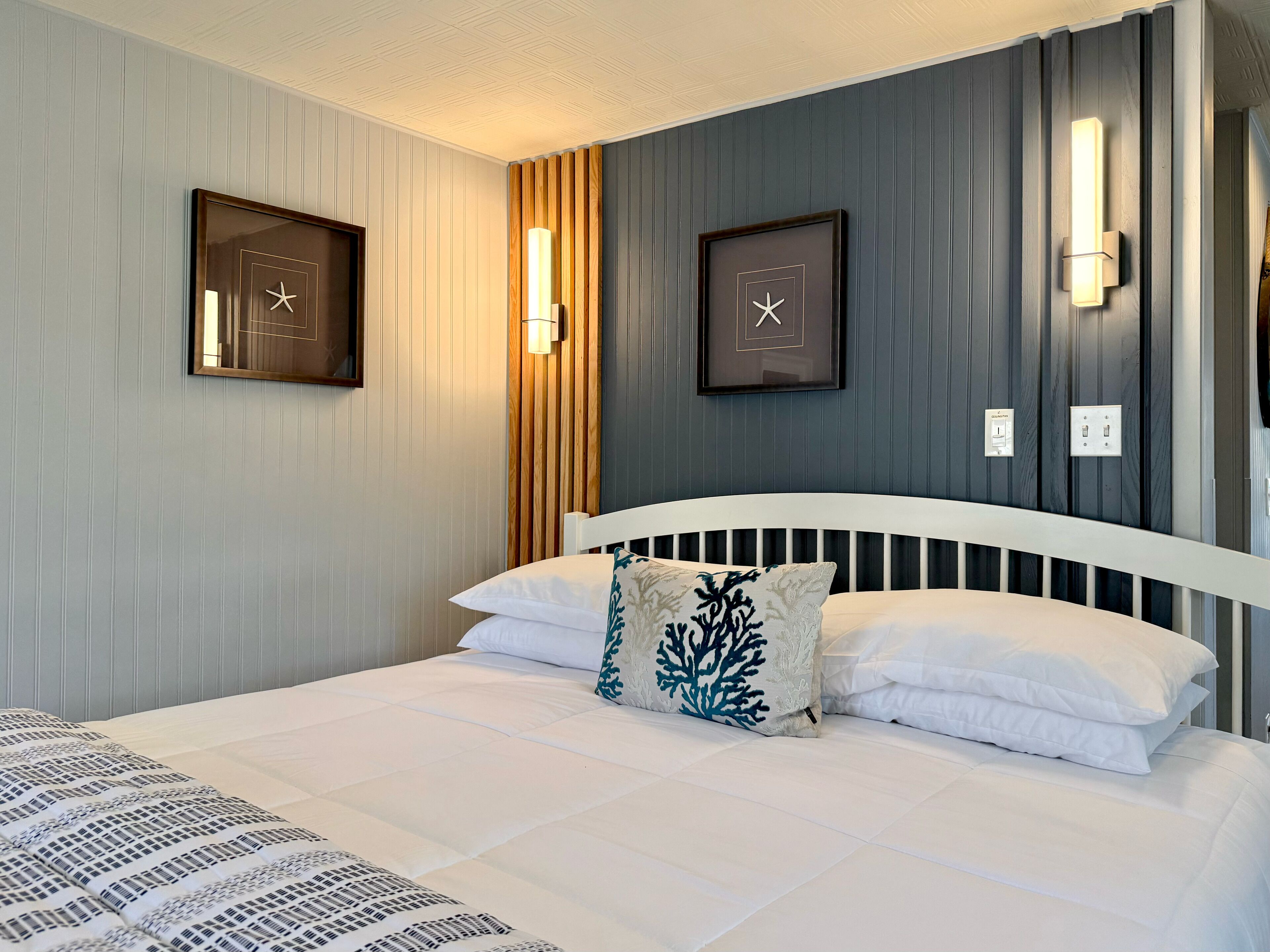 Ein Hotelzimmer mit einem weißen Bett, einem Zierkissen, Wanduhren und einer Holzpaneelausstattung.