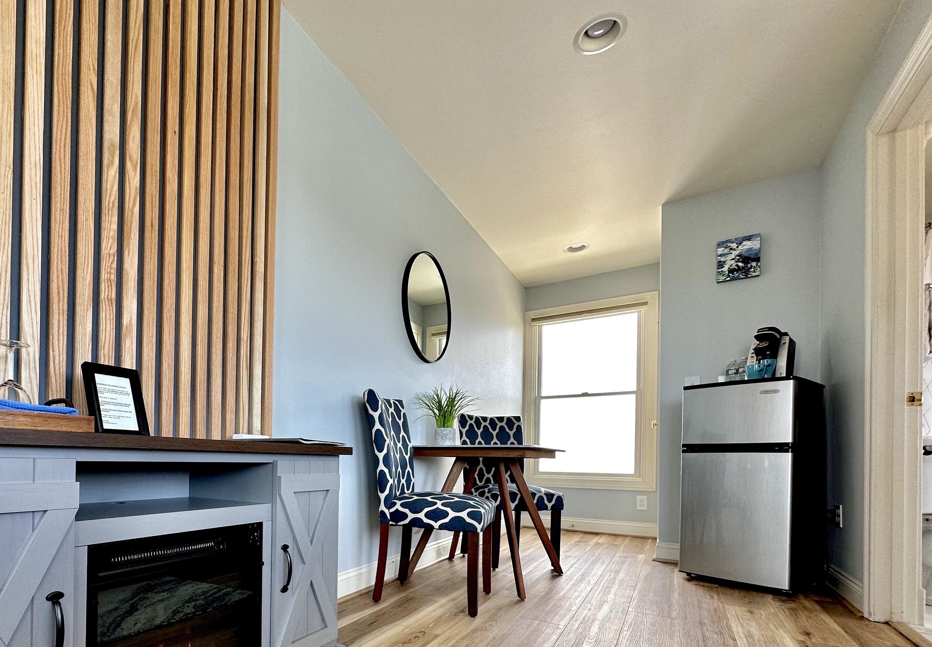 A compact kitchen with a built-in oven, a dining table with chairs, a refrigerator, and a window providing natural light.
