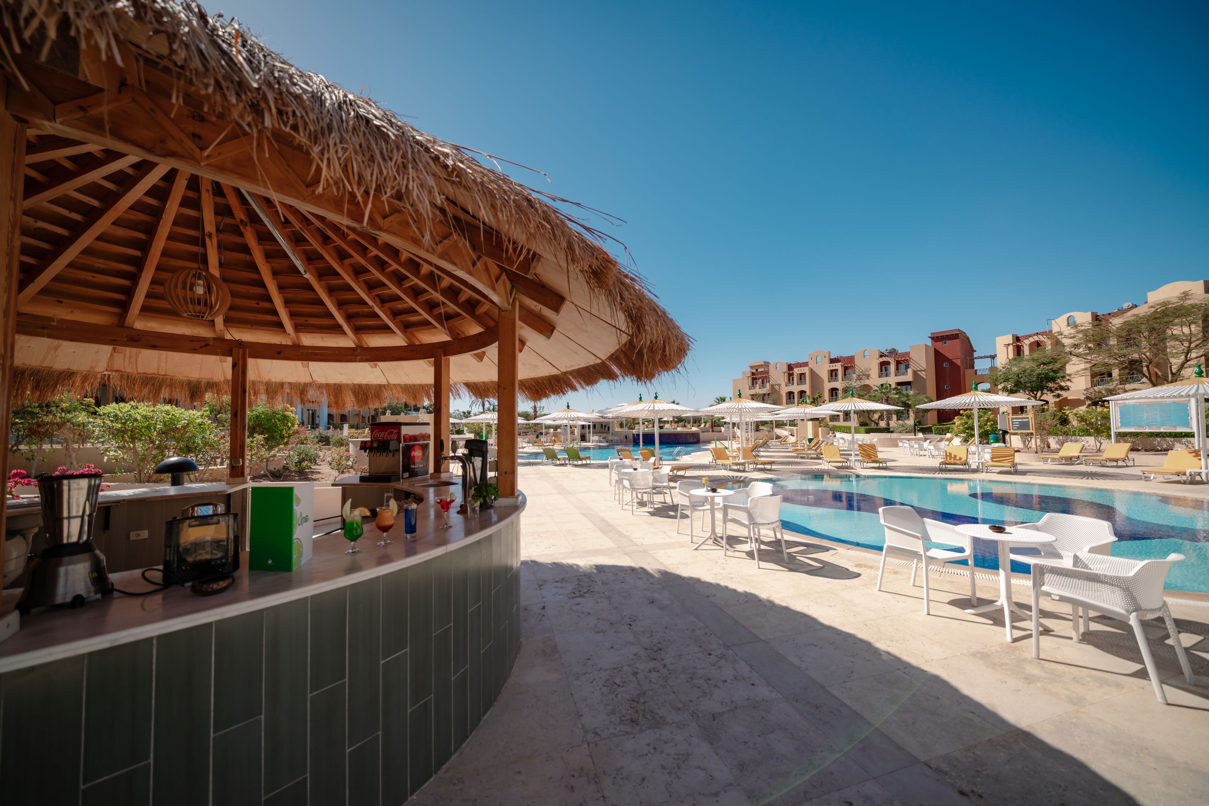 A poolside area with a bar, lounge chairs, and a thatched roof structure.