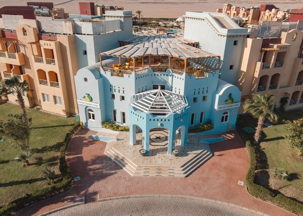 A large, multi-story hotel with a distinctive blue and beige color scheme, featuring a central courtyard with a fountain and outdoor seating area. -  Lemon & Soul Makadi Garden (Makadi Bay)