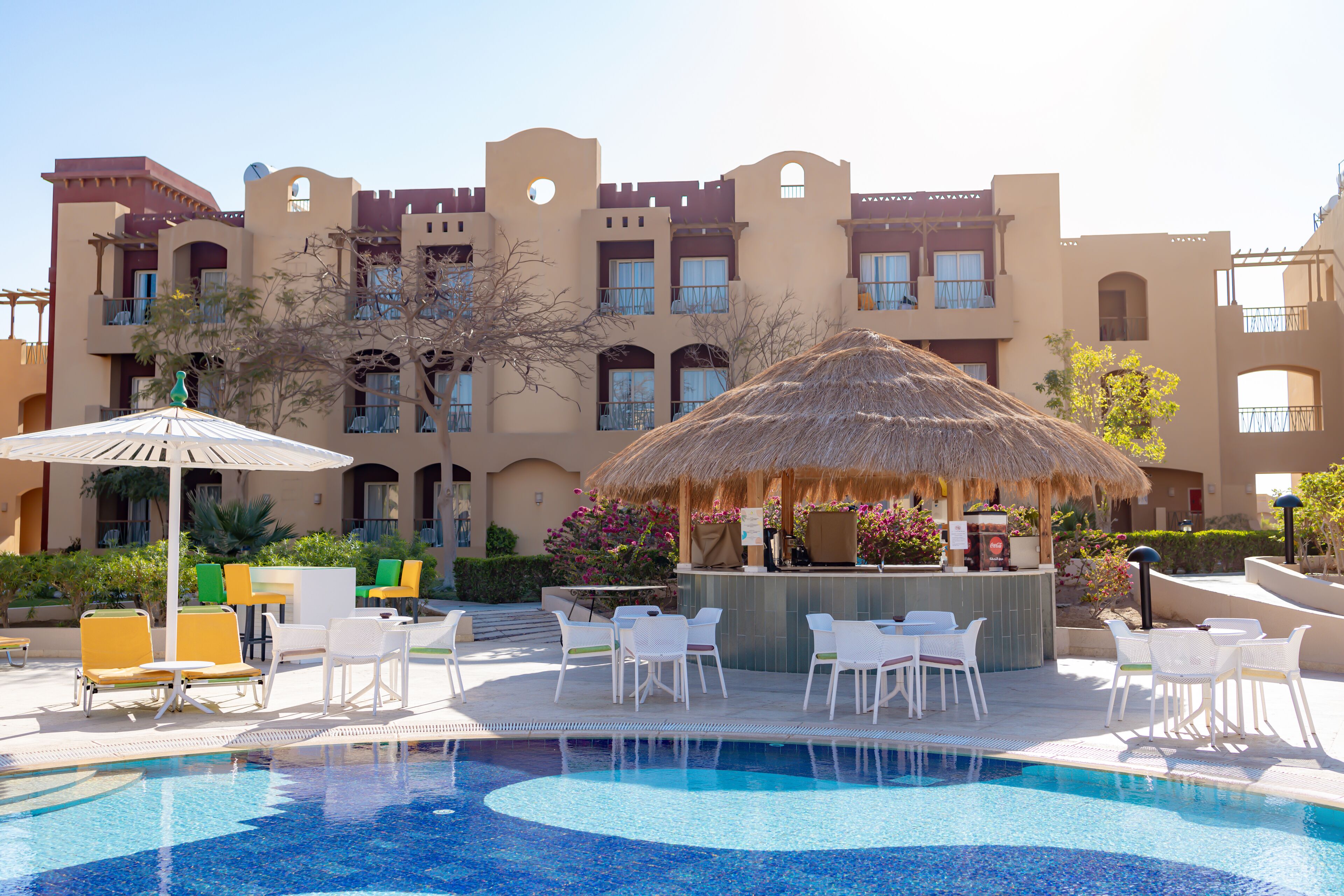 A swimming pool with lounge chairs and a bar area, surrounded by a building with multiple balconies and arched windows.