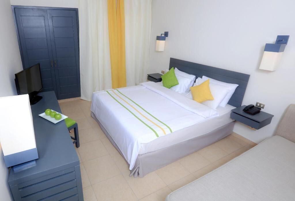 Una habitación de hotel con cama, mesitas de noche, un escritorio con silla, televisor y armario.