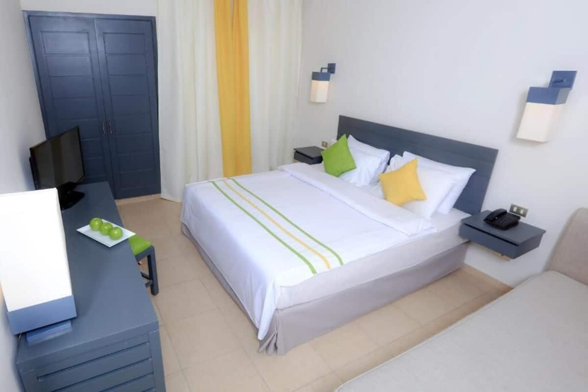 Ein Hotelzimmer mit Bett, Nachttischen, einem Schreibtisch mit Stuhl, einem Fernseher und einem Kleiderschrank.