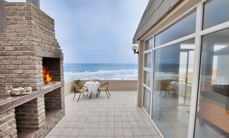 Un patio con chimenea de ladrillo, mobiliario exterior y vista al océano.