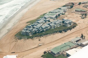 Vista aérea de una zona residencial costera con varias casas, una playa de arena y una carretera que conduce a la playa.