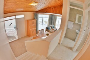 Amplia habitación con techo de madera, un comedor con mesa y sillas, y vistas al exterior a través de amplias ventanas.