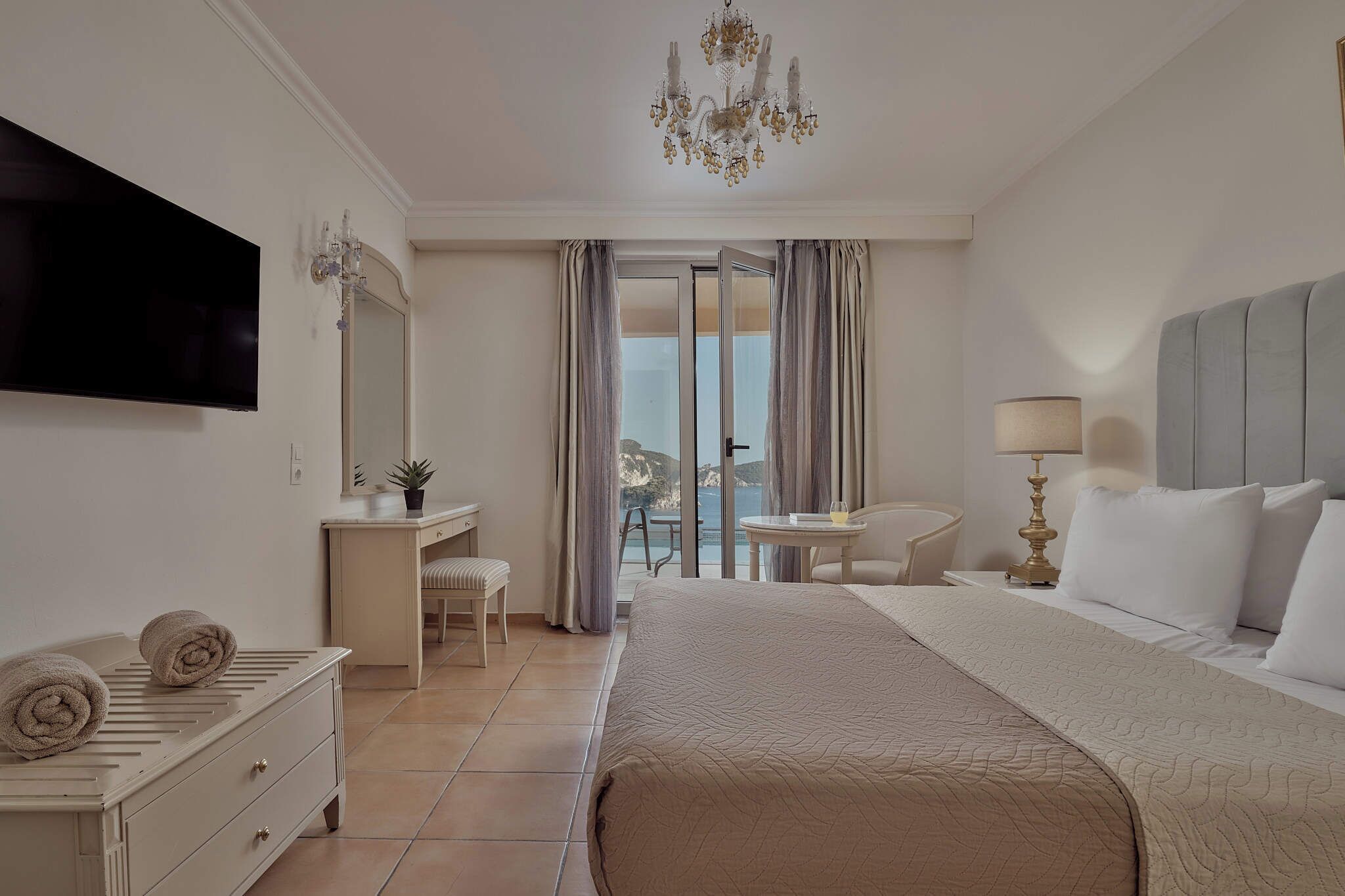 Une chambre d’hôtel avec un lit, un bureau, une chaise, une télévision et une vue sur la mer.