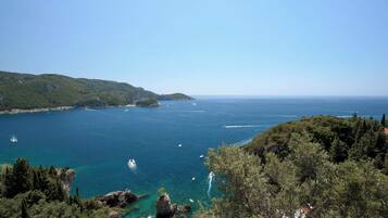 A coastal landscape with clear blue sea, rocky outcrops, and dense greenery.