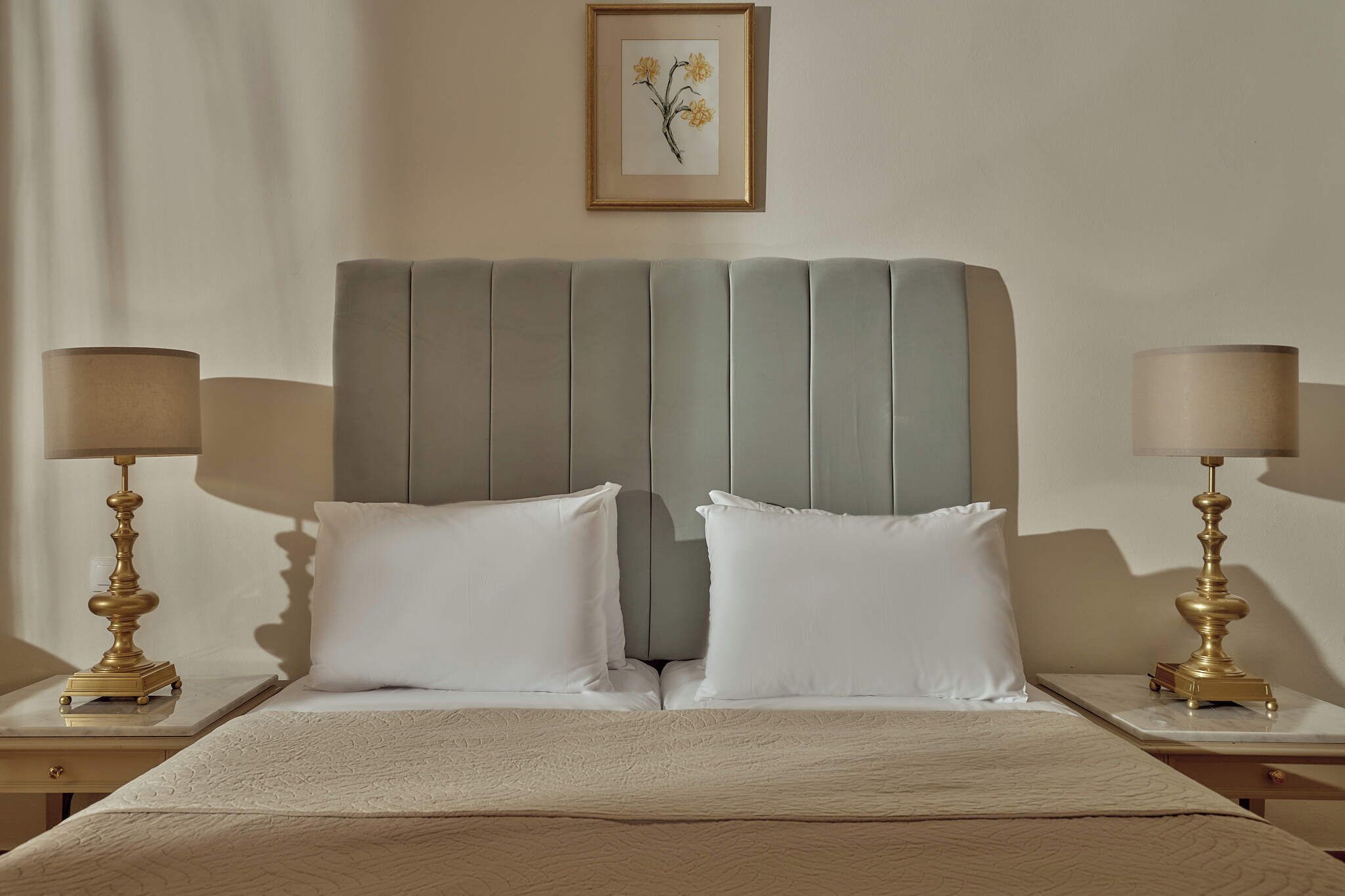Habitación de hotel con cama, dos mesitas de noche con lámparas, cabecero y un cuadro en la pared.