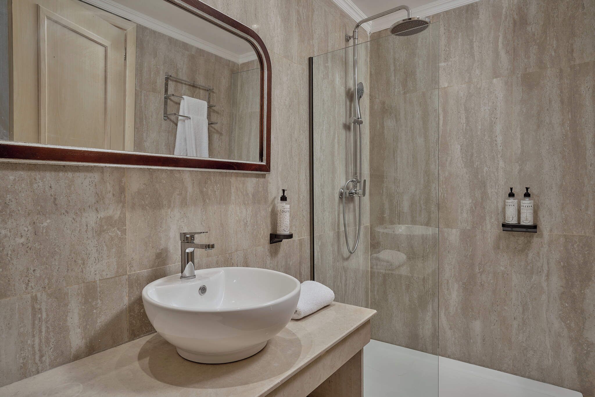 A bathroom with a large white sink, a glass shower enclosure, and a mirror with a wooden frame.