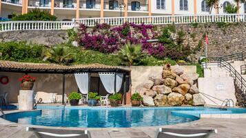 A hotel with a swimming pool, lounge chairs, and a garden with purple flowers.