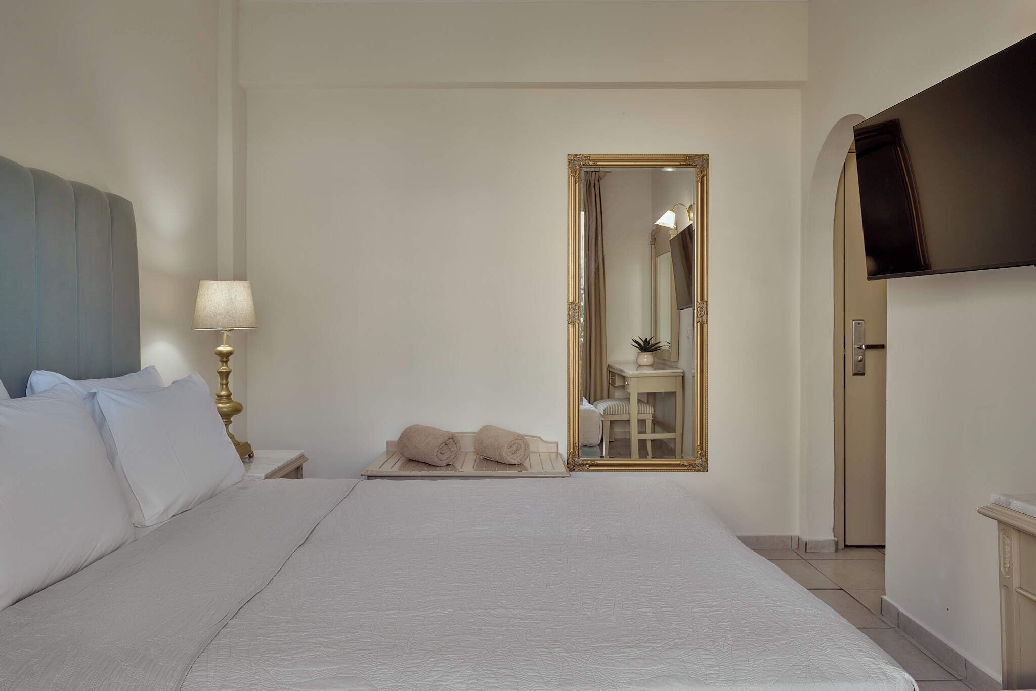 Une chambre d’hôtel avec un grand lit, une table de chevet avec une lampe, un miroir et un téléviseur fixé au mur.