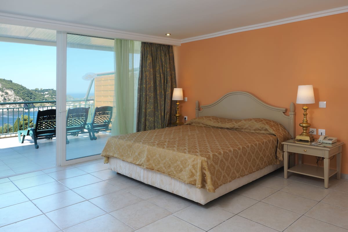 Une chambre à coucher avec un lit, deux tables de chevet avec des lampes, un balcon avec des chaises et une vue sur la mer.