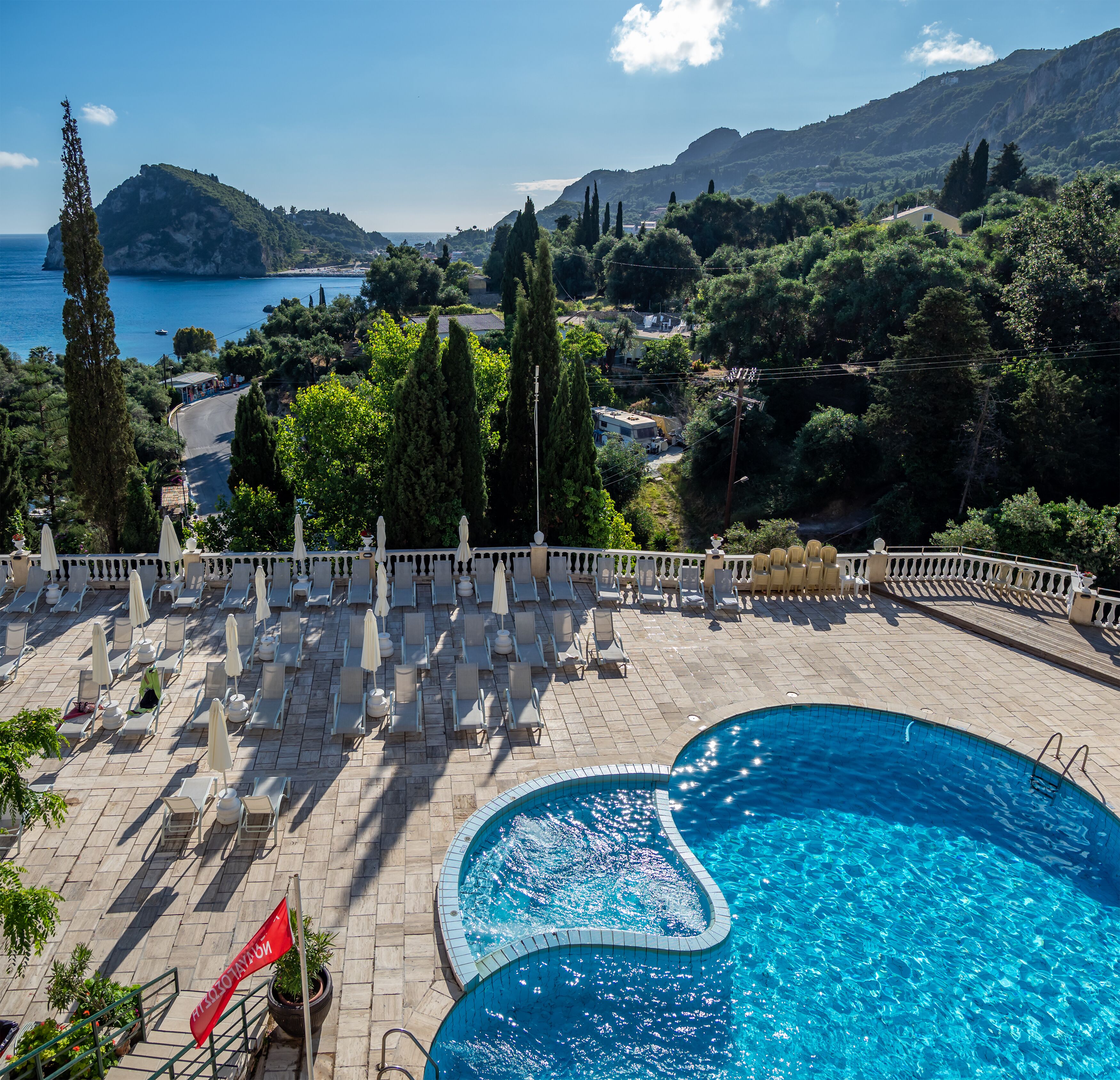 Un espace piscine doté de chaises longues et de parasols, offrant une vue panoramique sur un paysage magnifique, avec des montagnes et une étendue d’eau.
