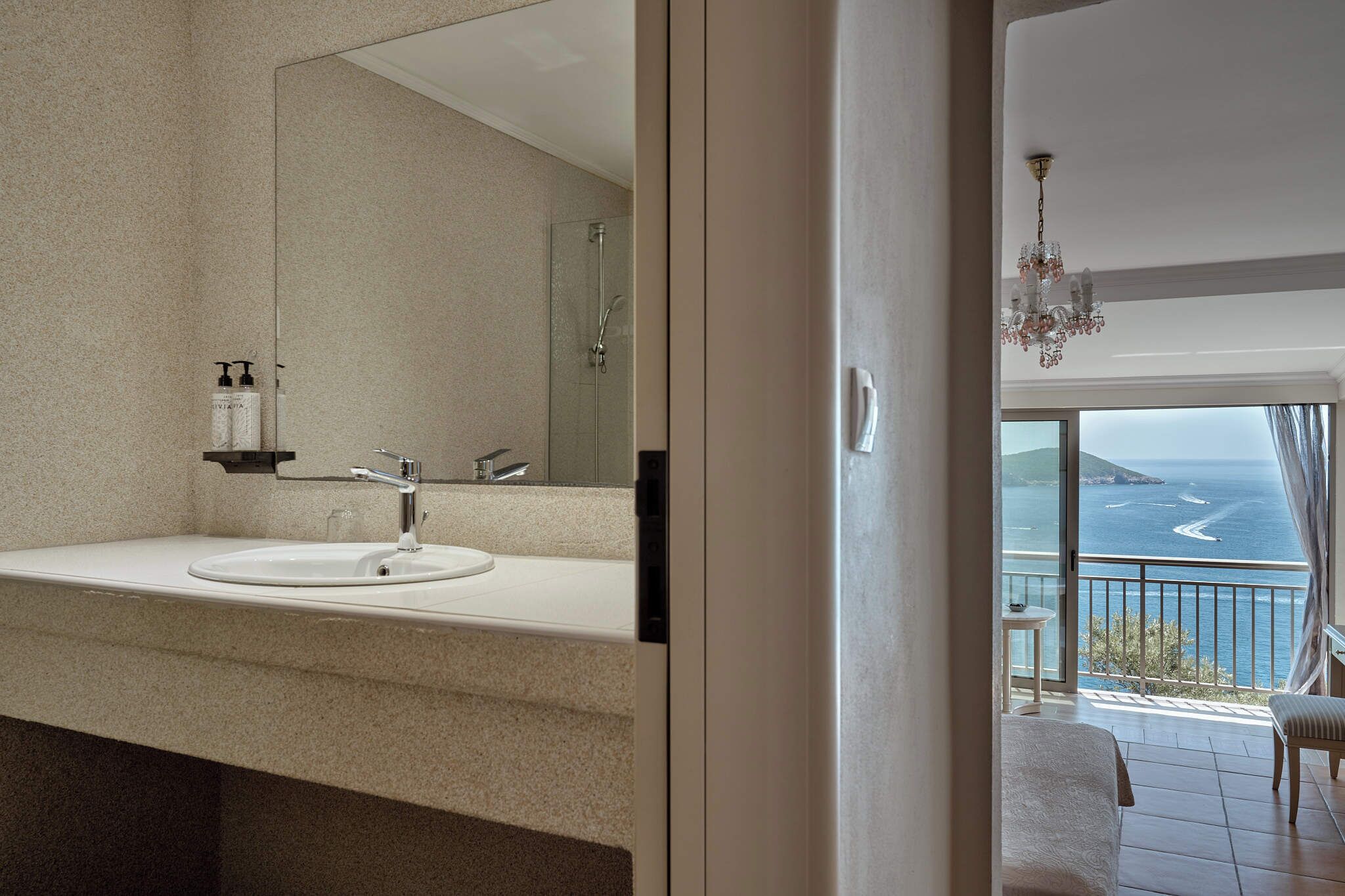 Un baño con un espejo grande, un lavabo y artículos de aseo. Hay un balcón con vista al mar.