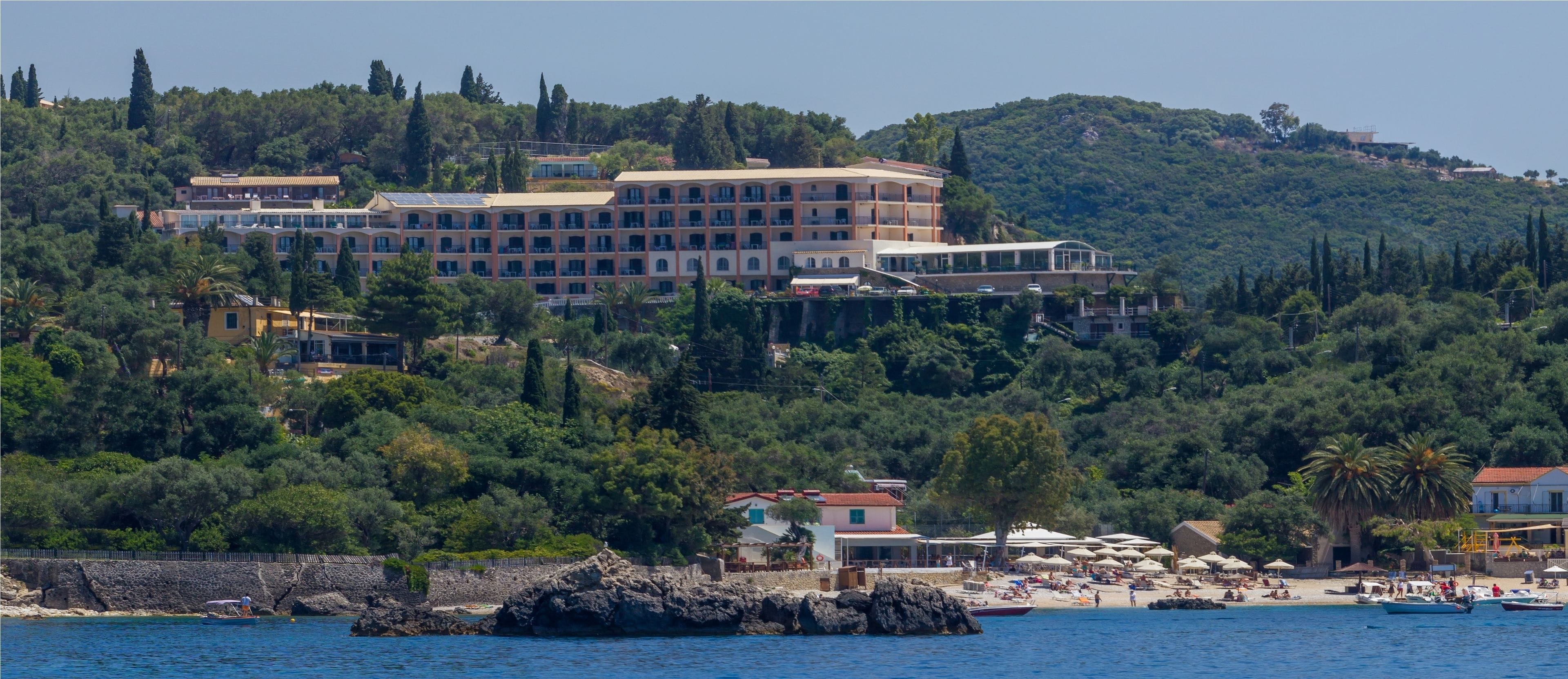 A coastal hotel with multiple buildings, a beach with umbrellas, and rocky outcrops.