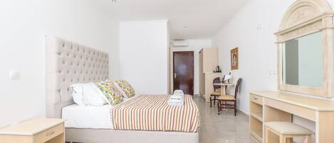 A bedroom with a large bed, a desk, a chair, and a mirror.